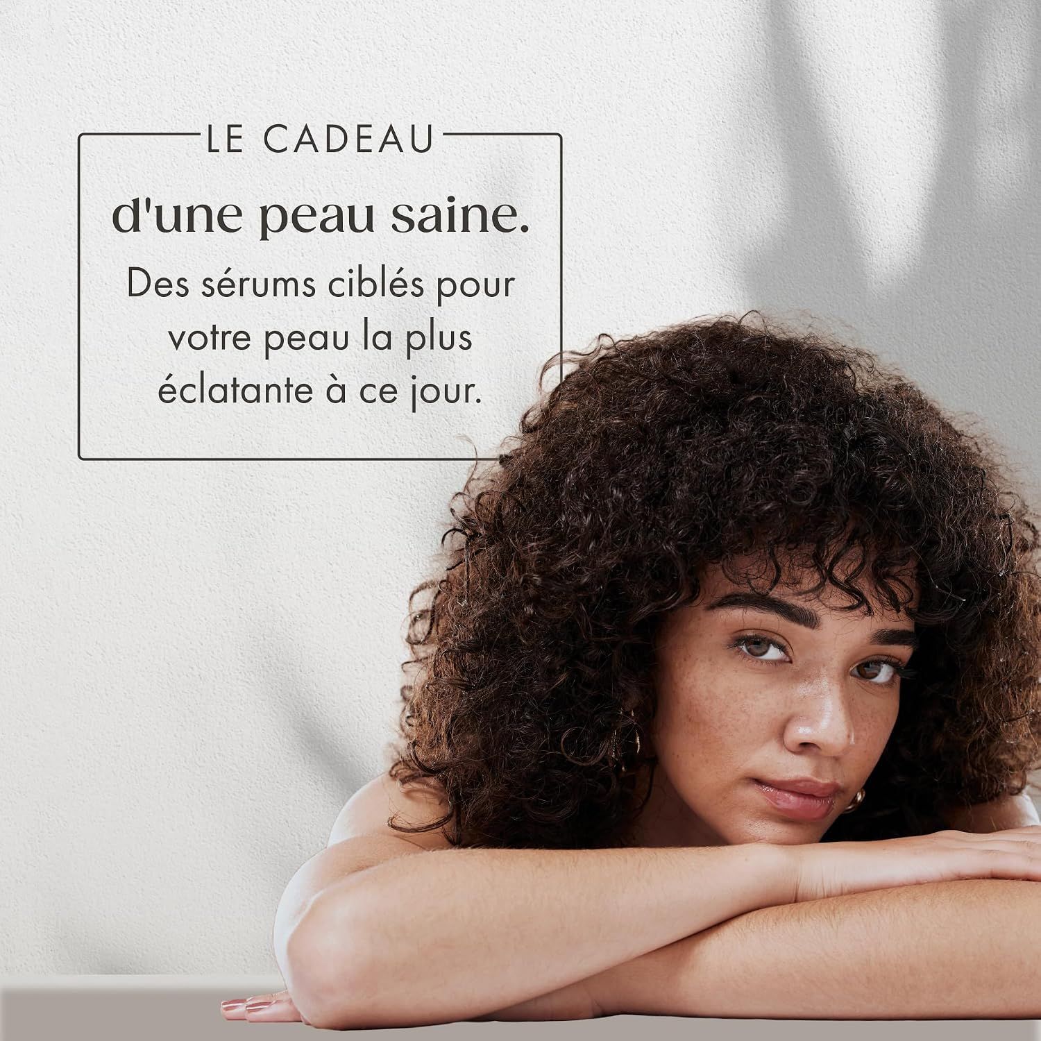 Femme aux cheveux bouclés regarde pensivement. Texte : Le cadeau d'une peau saine.