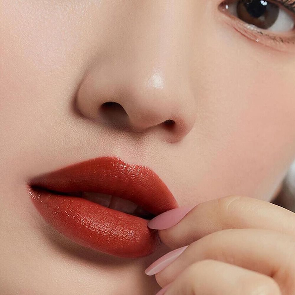 Close-up van lippen met rode lipgloss. Een hand met roze nagels raakt de lip aan.