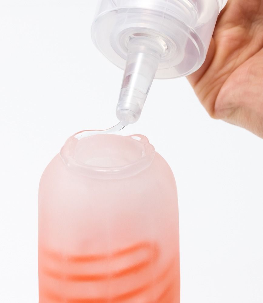 Vloeistof druppelt uit een tuit in een container. De container is roze en heeft een patroon.