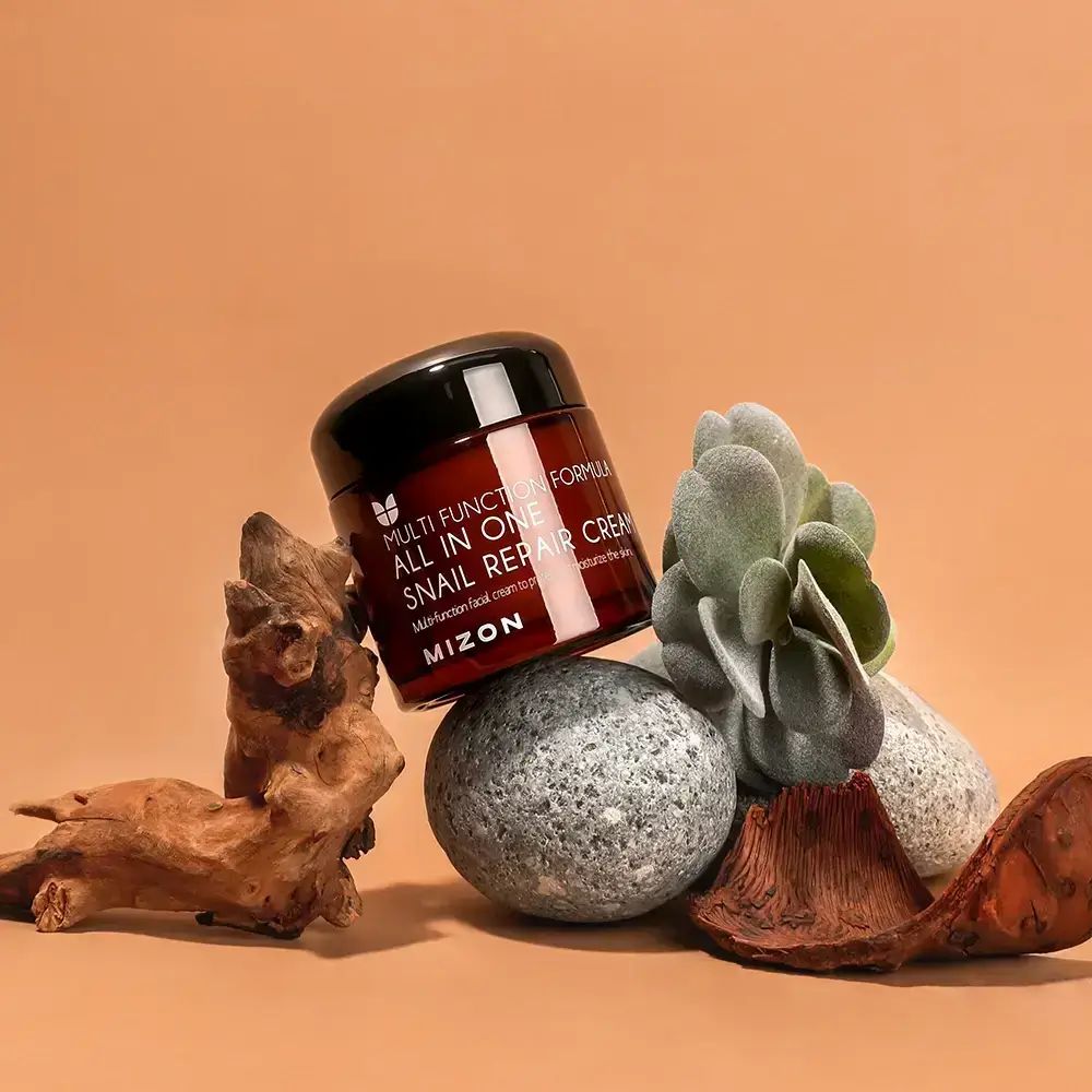 Bruine glazen pot met zwarte deksel. Opschrift: ALL IN ONE SNAIL REPAIR CREAM. Merk: MIZON. Decoratie.