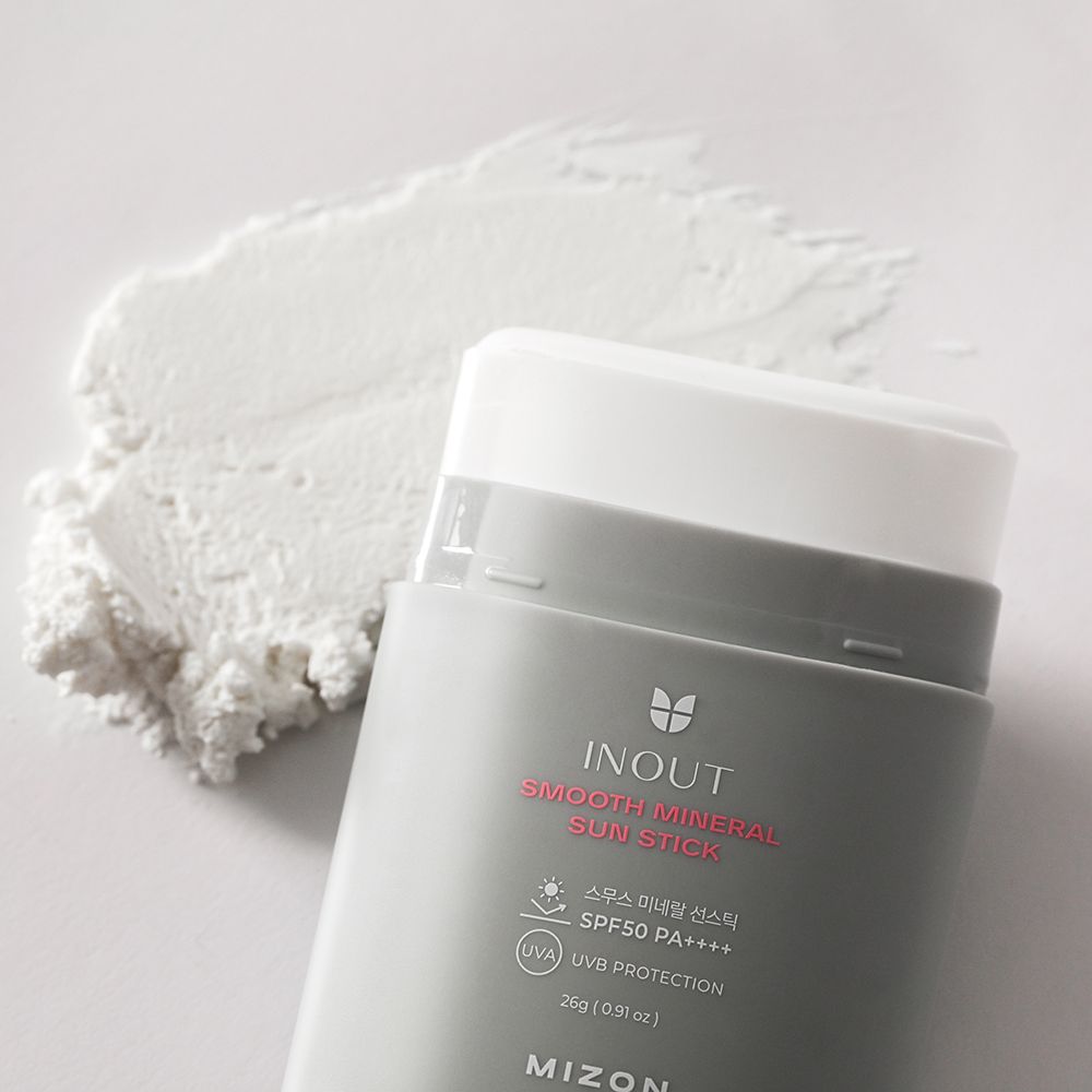 Grijze zonnebrandstick met witte dop en wit product ernaast. Opschrift: INOUT Smooth Mineral Sun Stick SPF50+ en MIZON.