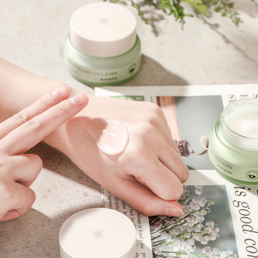 Main avec crème. À côté, pot de crème et couvercle. Sur papier journal et feuilles.