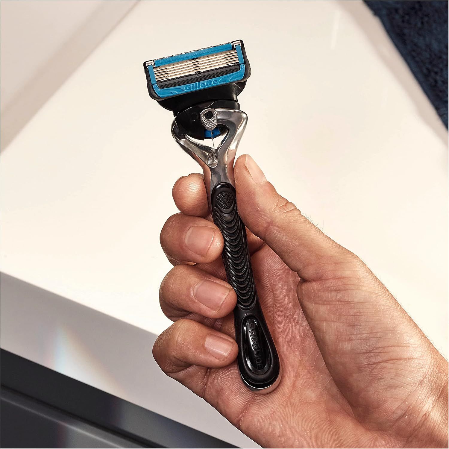 Een man houdt een Gillette scheermes met vijf bladen en een blauwe accent vast.