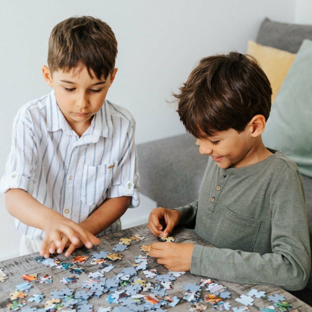 Deux garçons font un puzzle sur une table. Vue sur les mains et les pièces du puzzle. Différentes couleurs et formes des pièces.