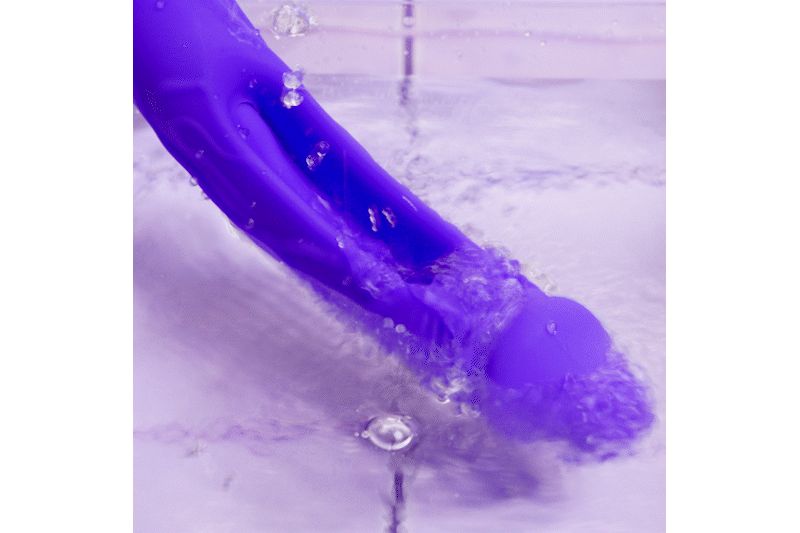 Vibrateur violet dans l'eau. L'eau éclabousse le vibrateur. Le vibrateur est partiellement immergé.
