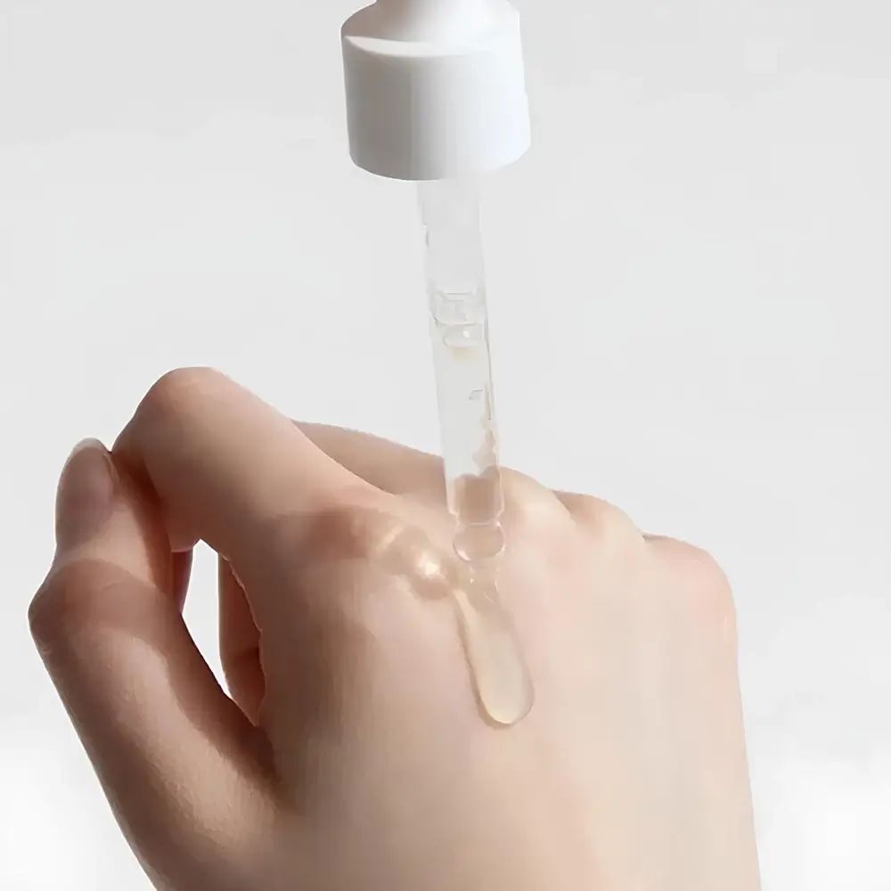 Main avec gouttes d'essence. Pipette distribuant du liquide sur la peau. Liquide clair.