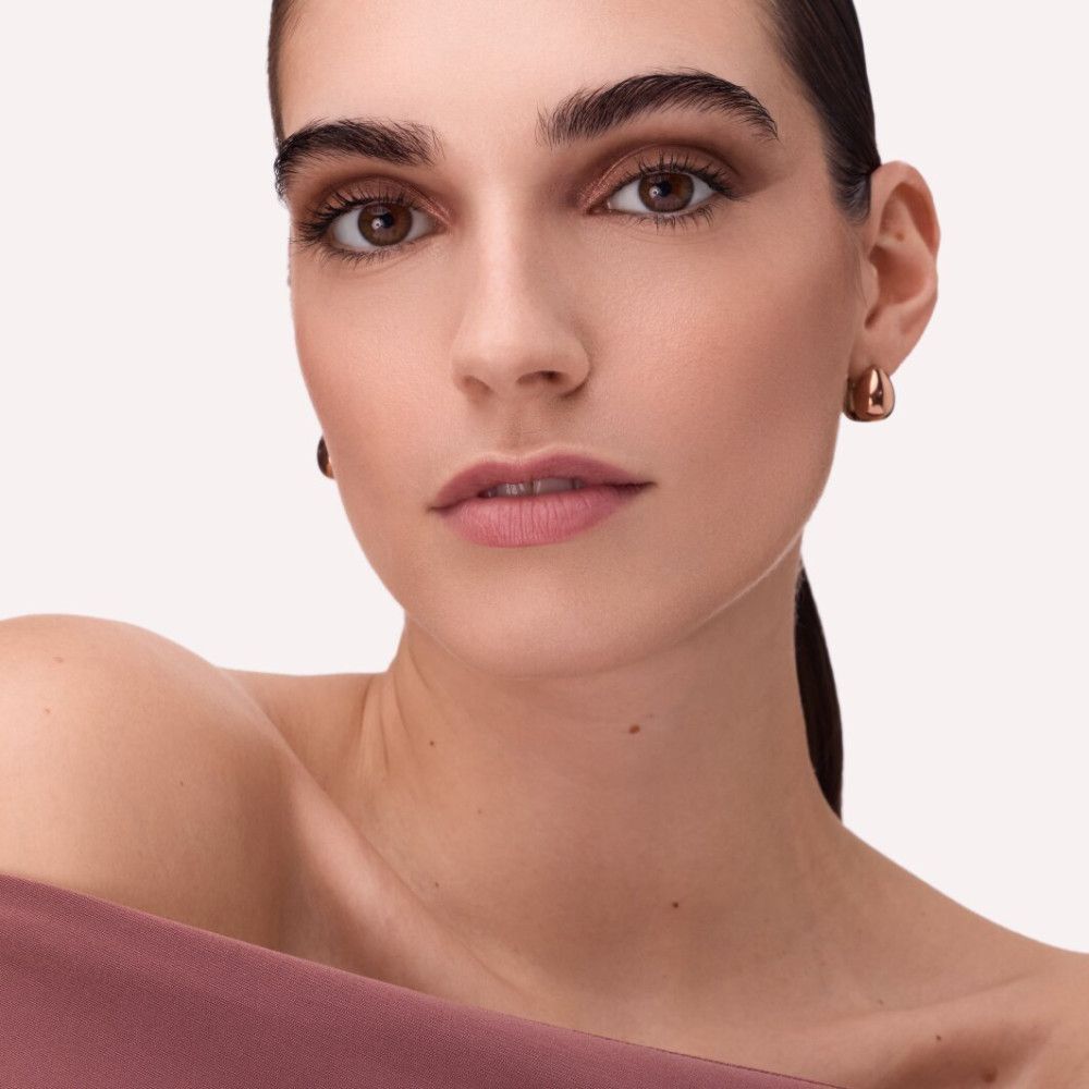 Close-up van een vrouw met make-up. Focus op ogen en lippen. Huidtint, roze lippen, subtiele oogmake-up.