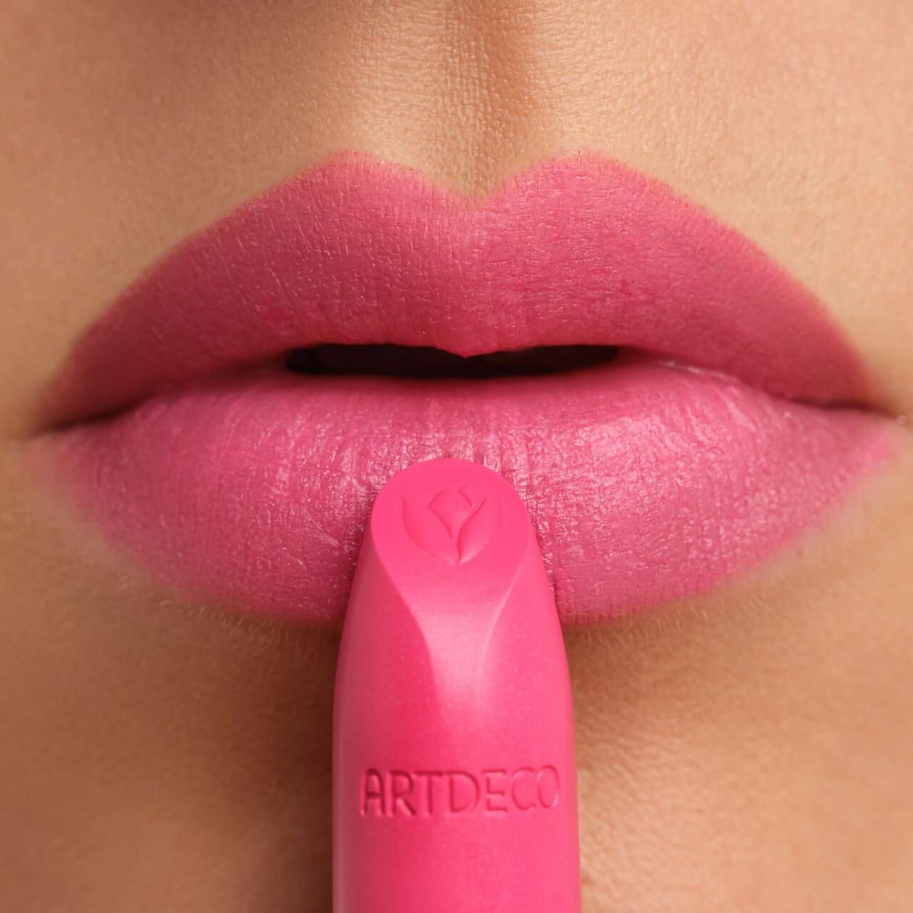 Close-up van lippen beschilderd met roze lipstick. De lipstick is voor de lippen te zien. ARTDECO is zichtbaar.