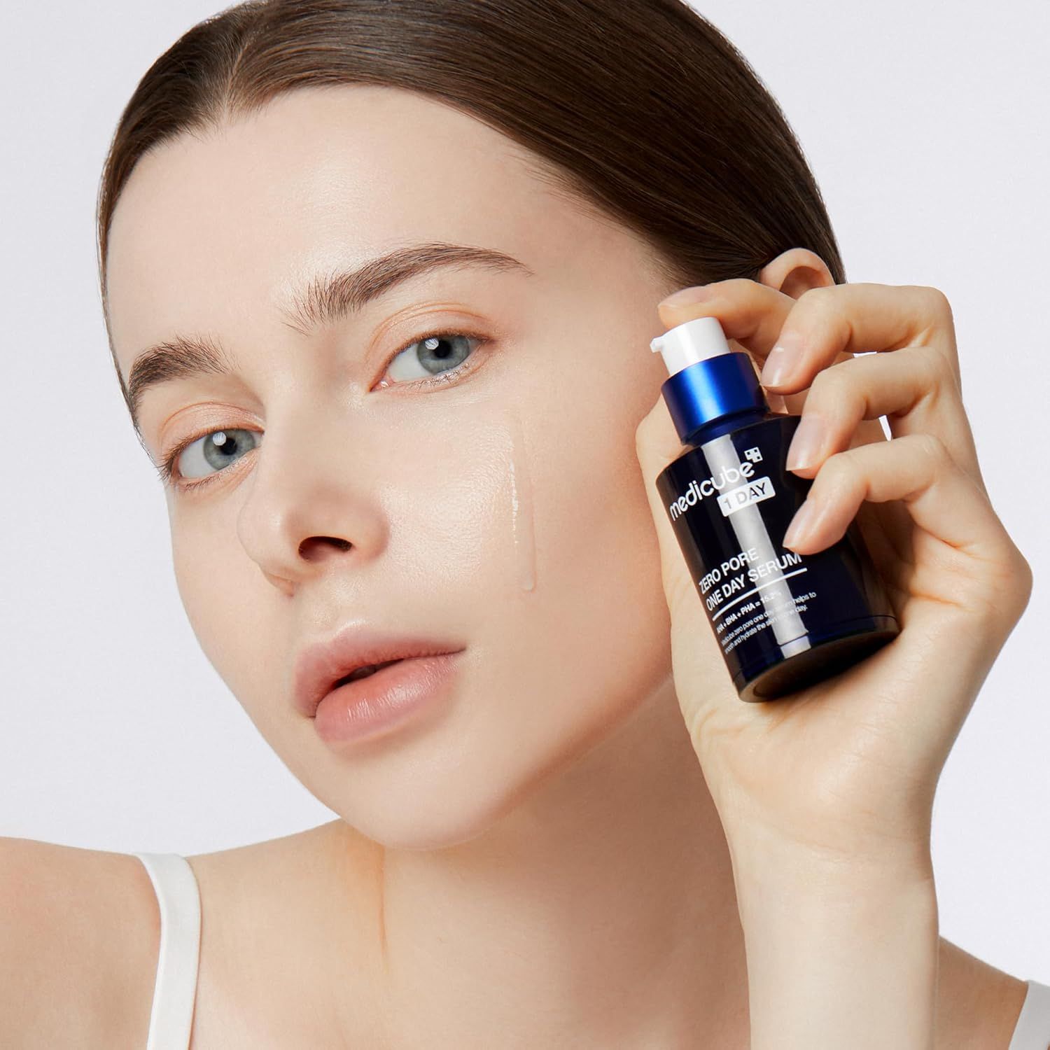 Vrouw houdt een flesje MEDICUBE Zero Pore One Day Serum vast. Product wordt op de huid aangebracht. Blauwe dop, zwarte fles.