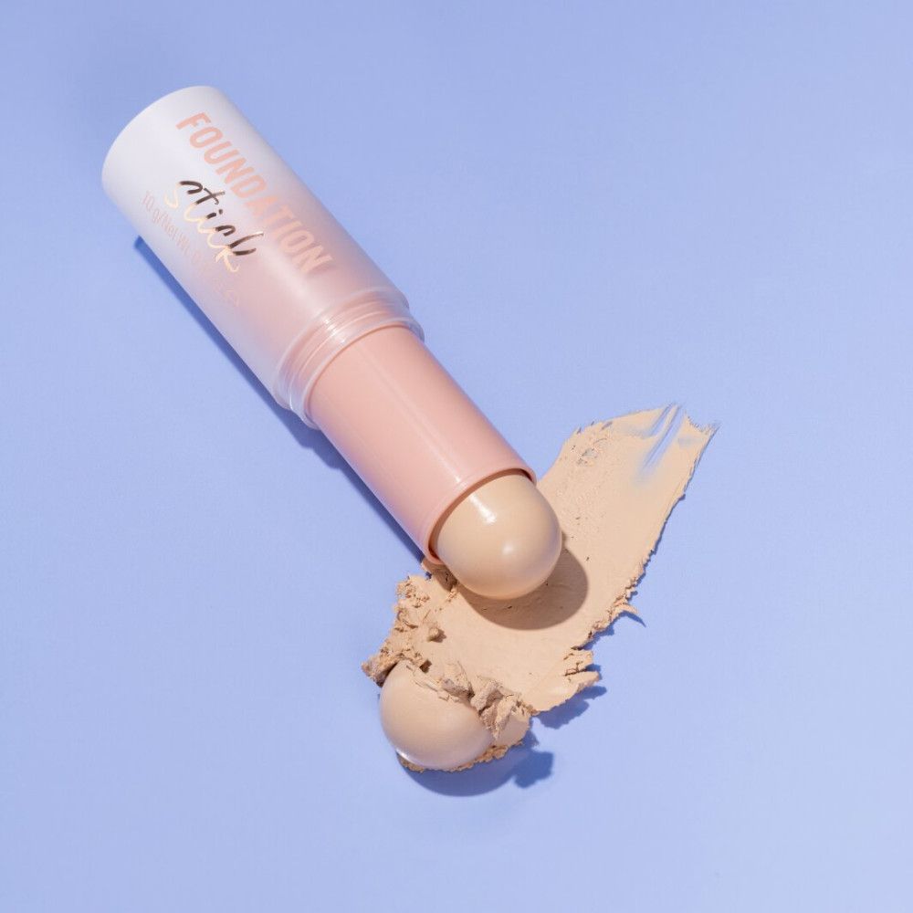 Stick de fond de teint et tache de fond de teint sur fond bleu. Le stick est rose et blanc.