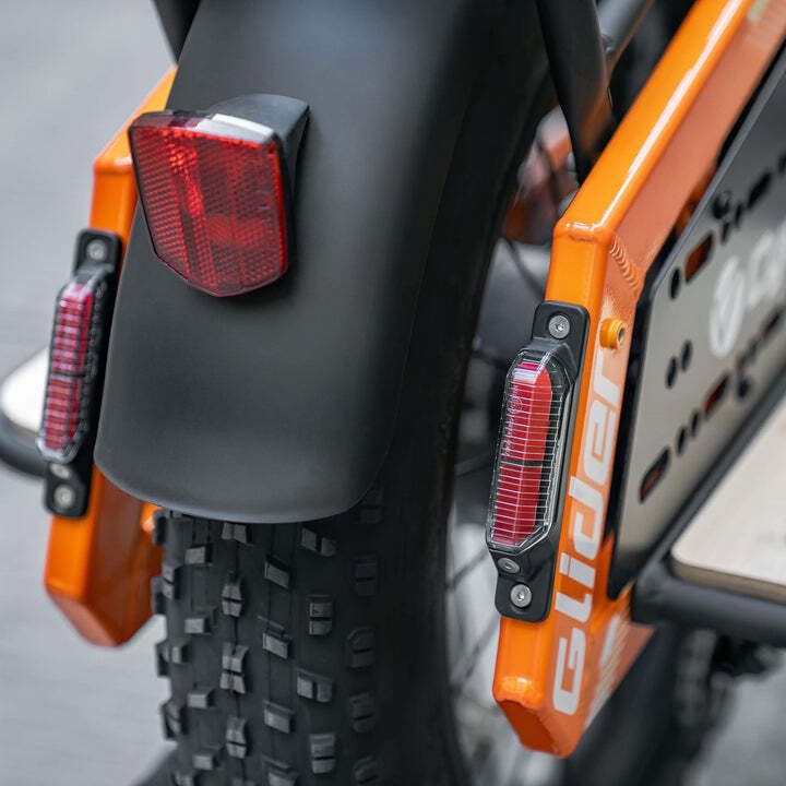 Achterlicht en spatbord van een oranje fiets. Twee rode lichten en zwarte spatbord.