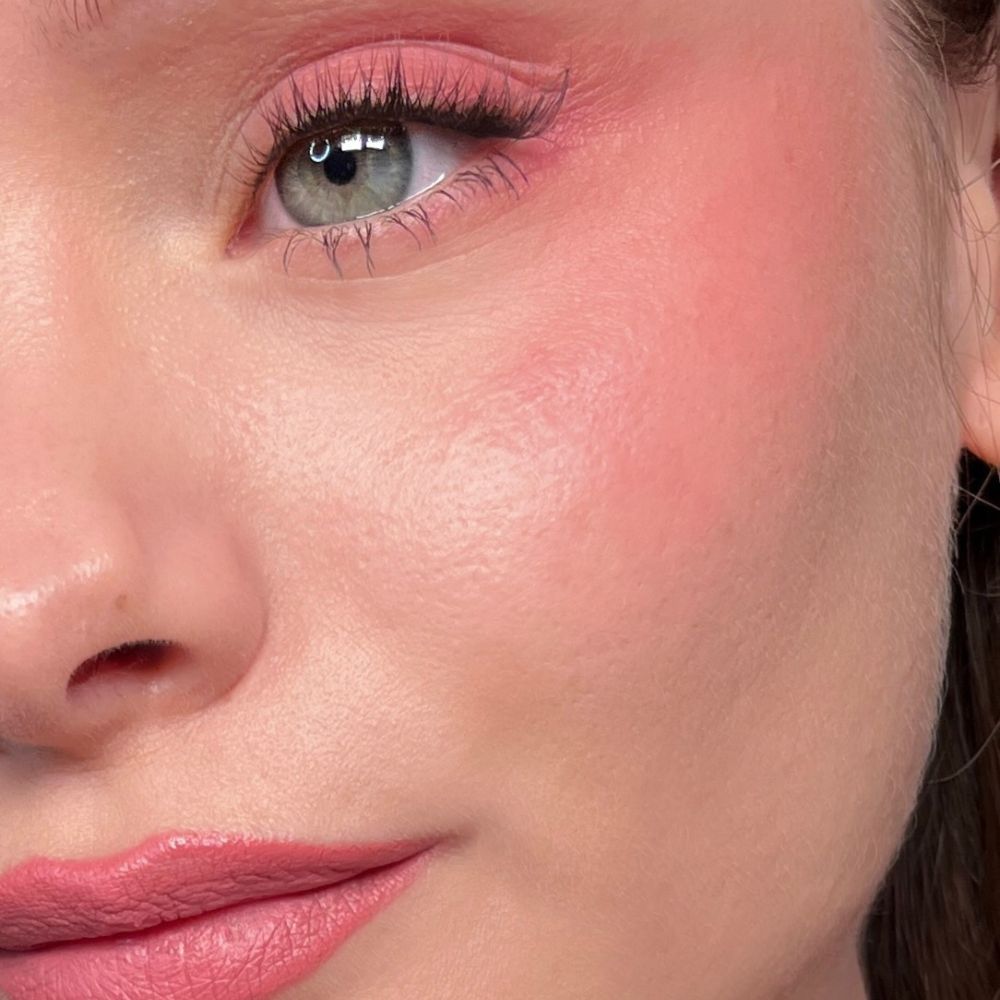 Gros plan d'un visage avec maquillage rose sur les yeux, les joues et les lèvres. Yeux verts.