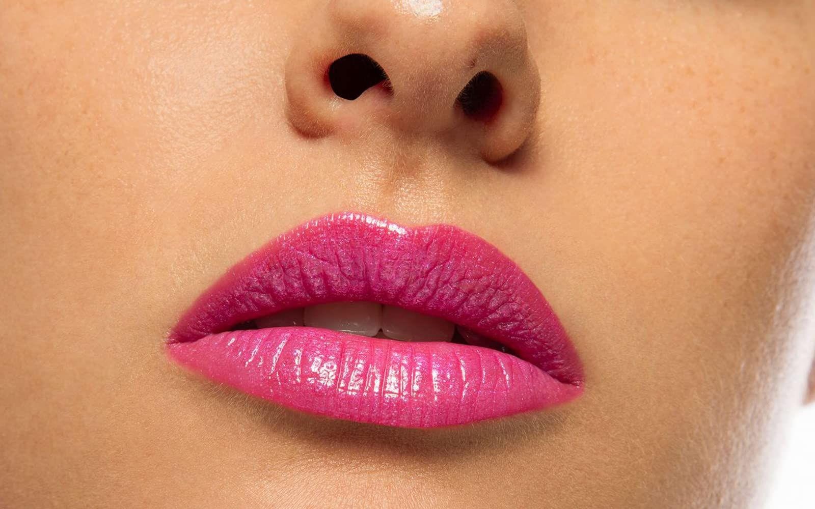 Gros plan sur des lèvres maquillées avec un rouge à lèvres rose. Lèvres ouvertes, dents visibles. Peau autour.