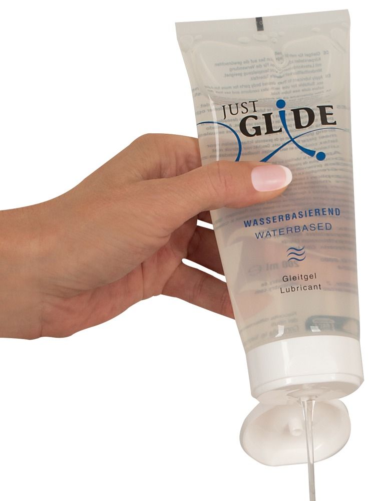 Tube de gel lubrifiant tenu par une main. Inscription: Just Glide, à base d'eau. Du gel coule du tube.
