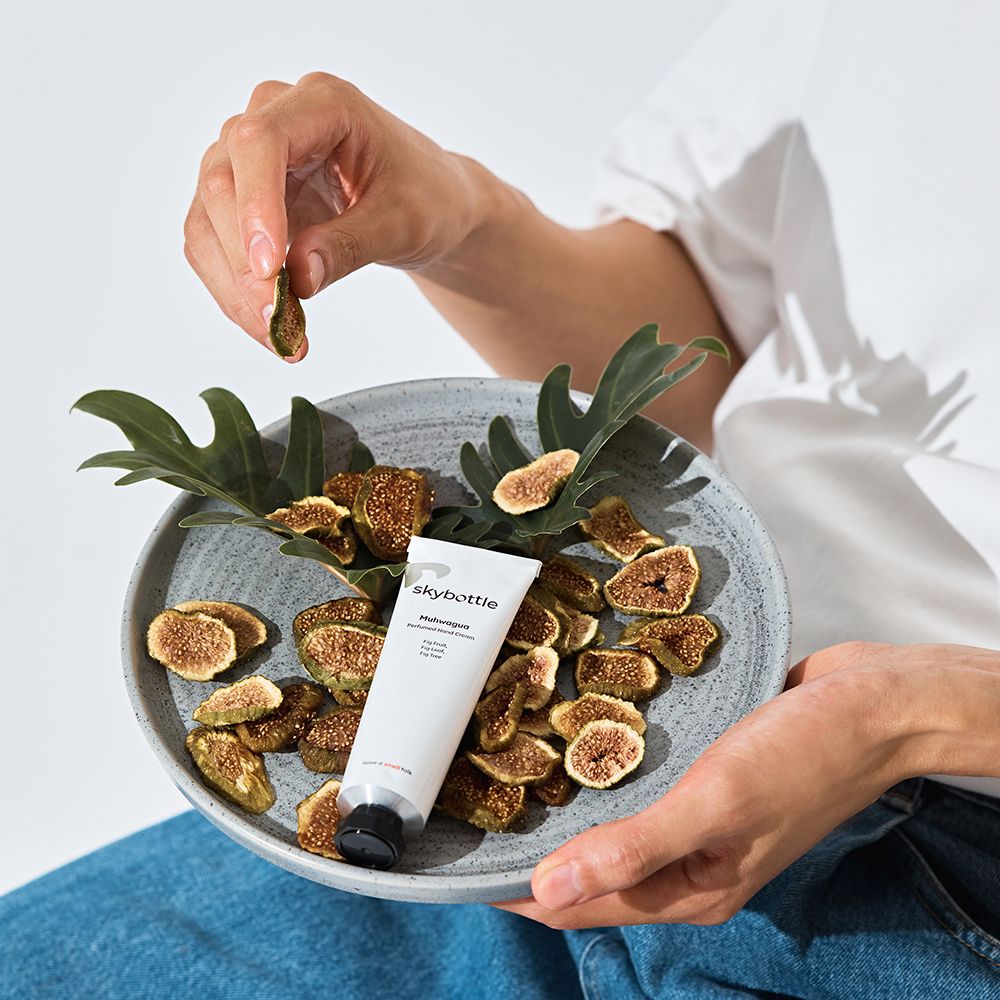 Personne tenant une figue séchée au-dessus d'un bol avec des figues et des feuilles. Un tube est dans le bol.