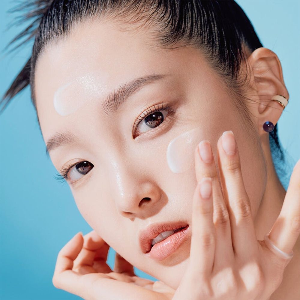 Femme appliquant de la crème solaire sur son visage. Produit non identifiable.