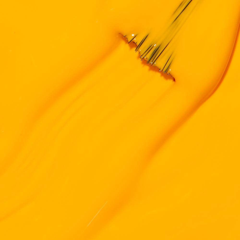 Coup de pinceau de vernis à ongles jaune. Les poils sont visibles. Le vernis est brillant.