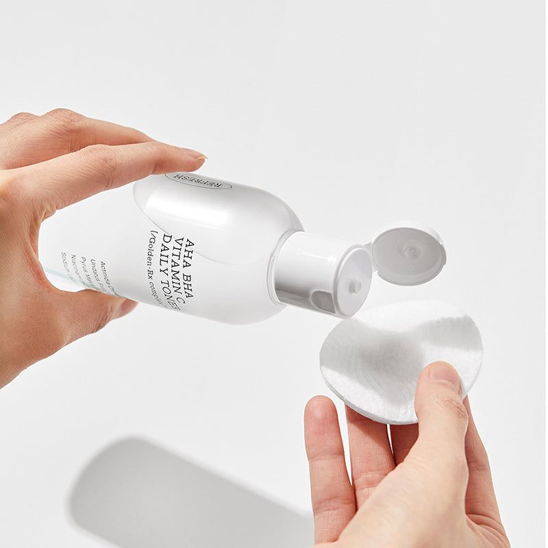 Flacon blanc de toner versé sur un coton. Inscription : AHA BHA Vitamin C Daily Toner.