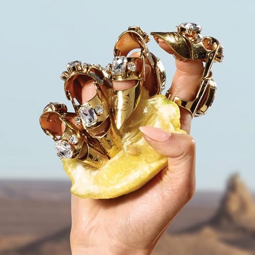 Hand met gouden ringen met edelstenen, houdt een stuk citroen vast. Achtergrond: landschap.