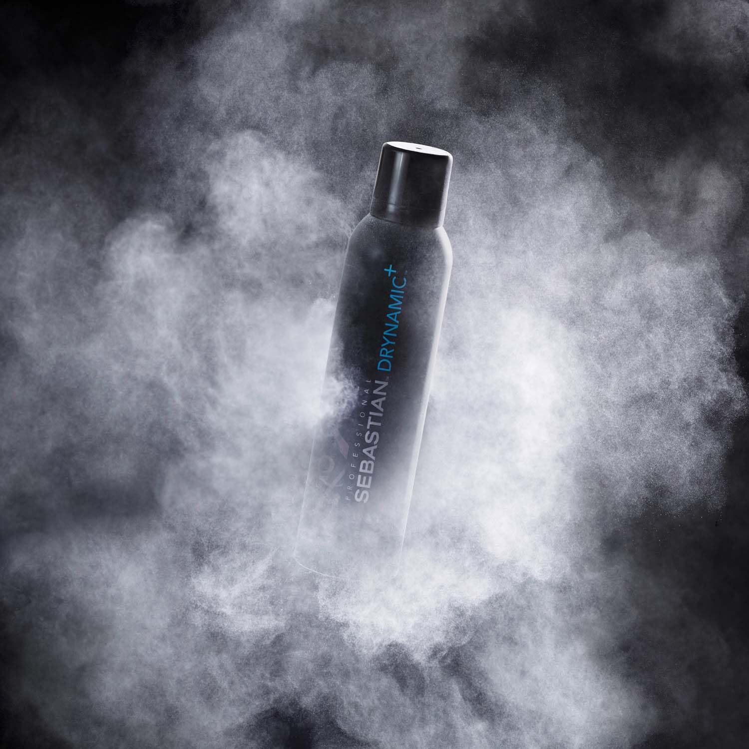 Flacon aérosol Sebastian Drynamic+ dans un nuage de poussière.