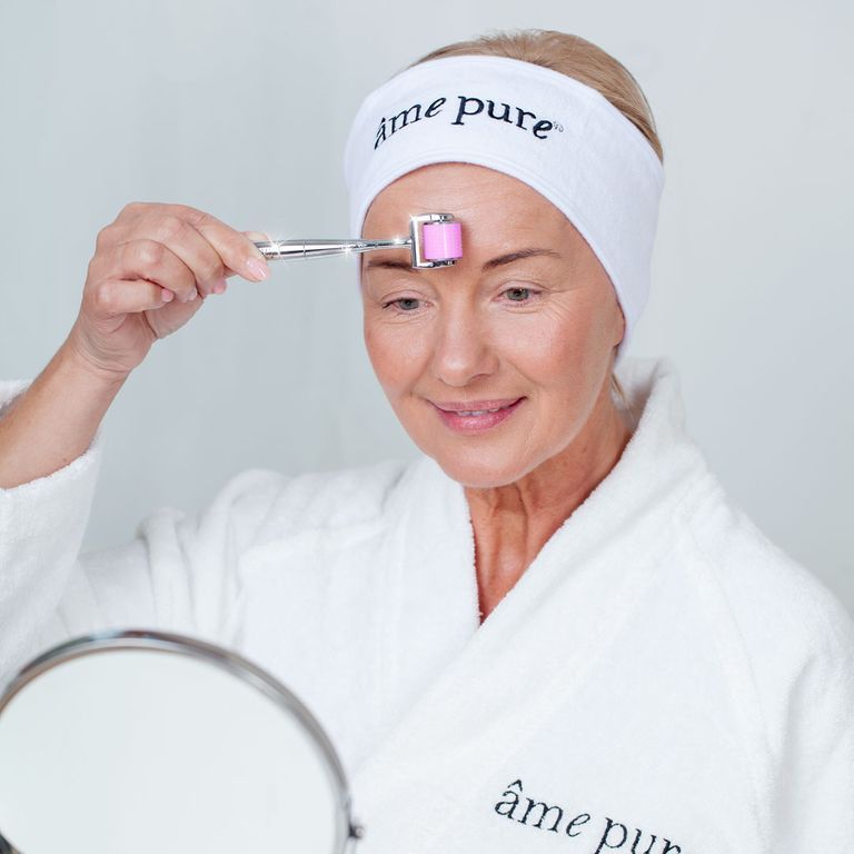 Vrouw met hoofdband gebruikt microneedling gezichtsroller op het voorhoofd.