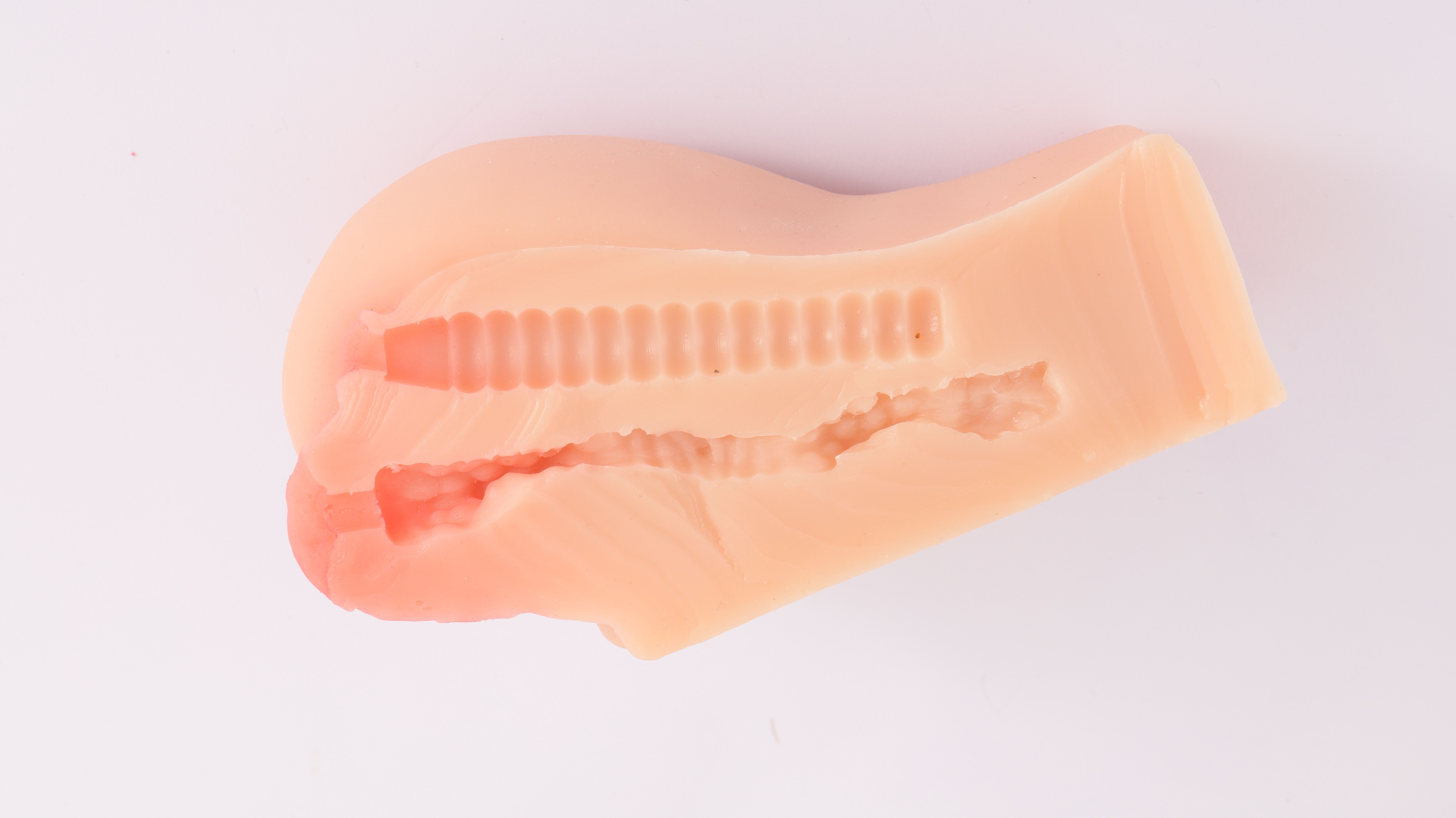 Huidkleurig, anatomisch gevormd product met interne structuren. Getoond op witte achtergrond.