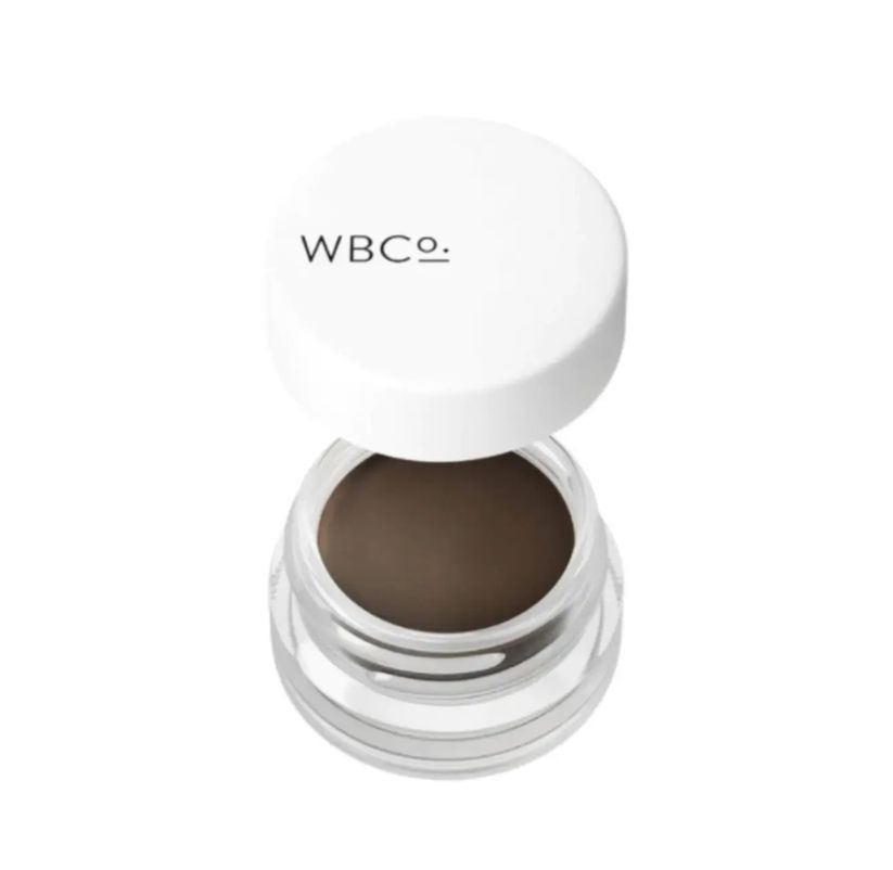 Pommade à sourcils dans un pot transparent avec un couvercle blanc. "WBCo." est écrit sur le couvercle.