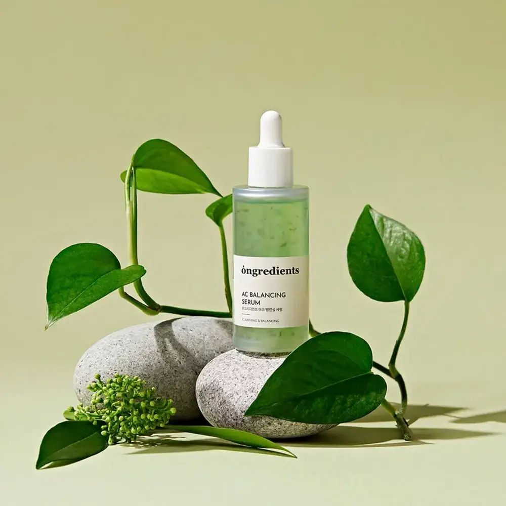 Serumfles op stenen met bladeren. Opschrift: Ongredients AC Balancing Serum. Groene vloeistof.