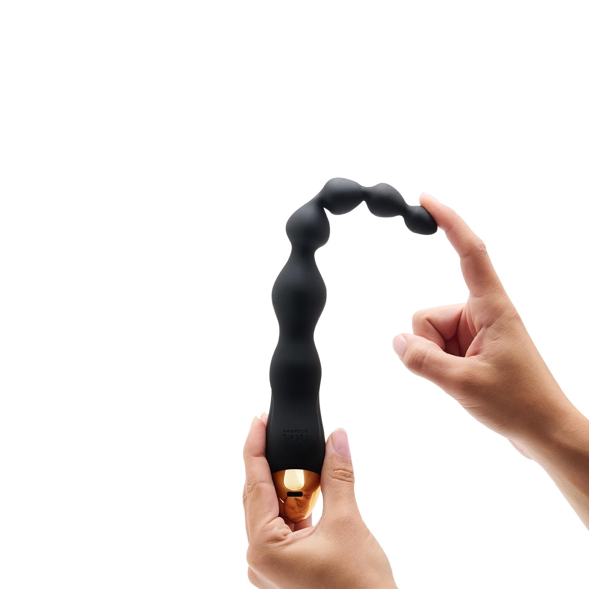 Zwarte vibrerende anale ketting, gedeeltelijk gebogen, vastgehouden door handen. Gouden uiteinde zichtbaar.