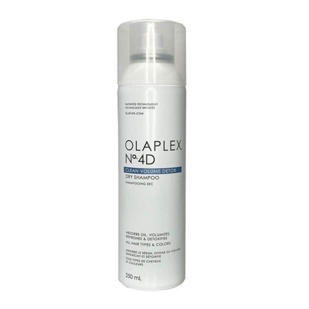 Main vaporisant le shampooing sec Olaplex Nº4D. Fond bleu. Brouillard de pulvérisation visible.