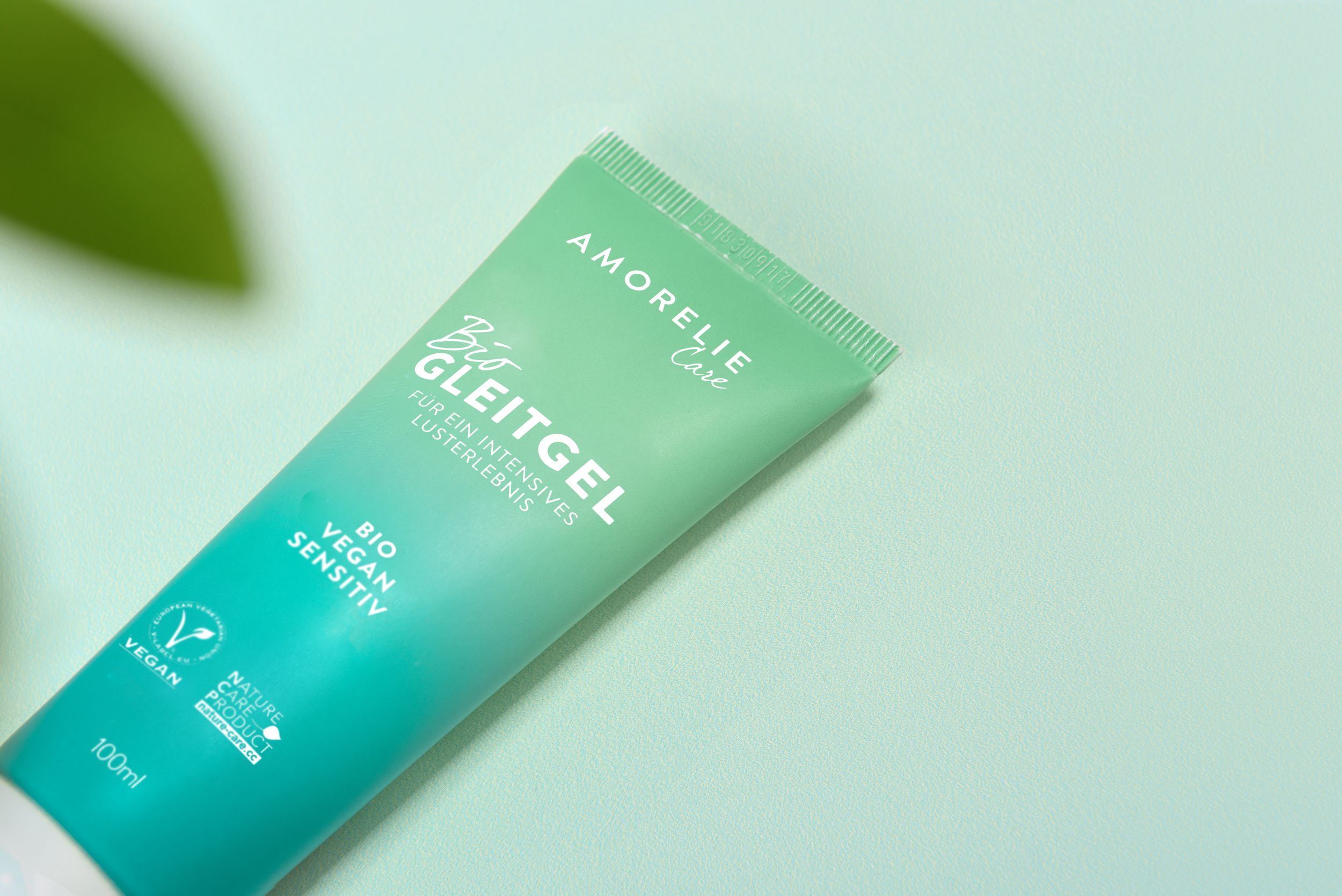 Close-up van een groene tube. Opschrift: AMORELIE Care, Bio Gleitgel, Bio Vegan Sensitiv. Vegan-keurmerk. Groene achtergrond.