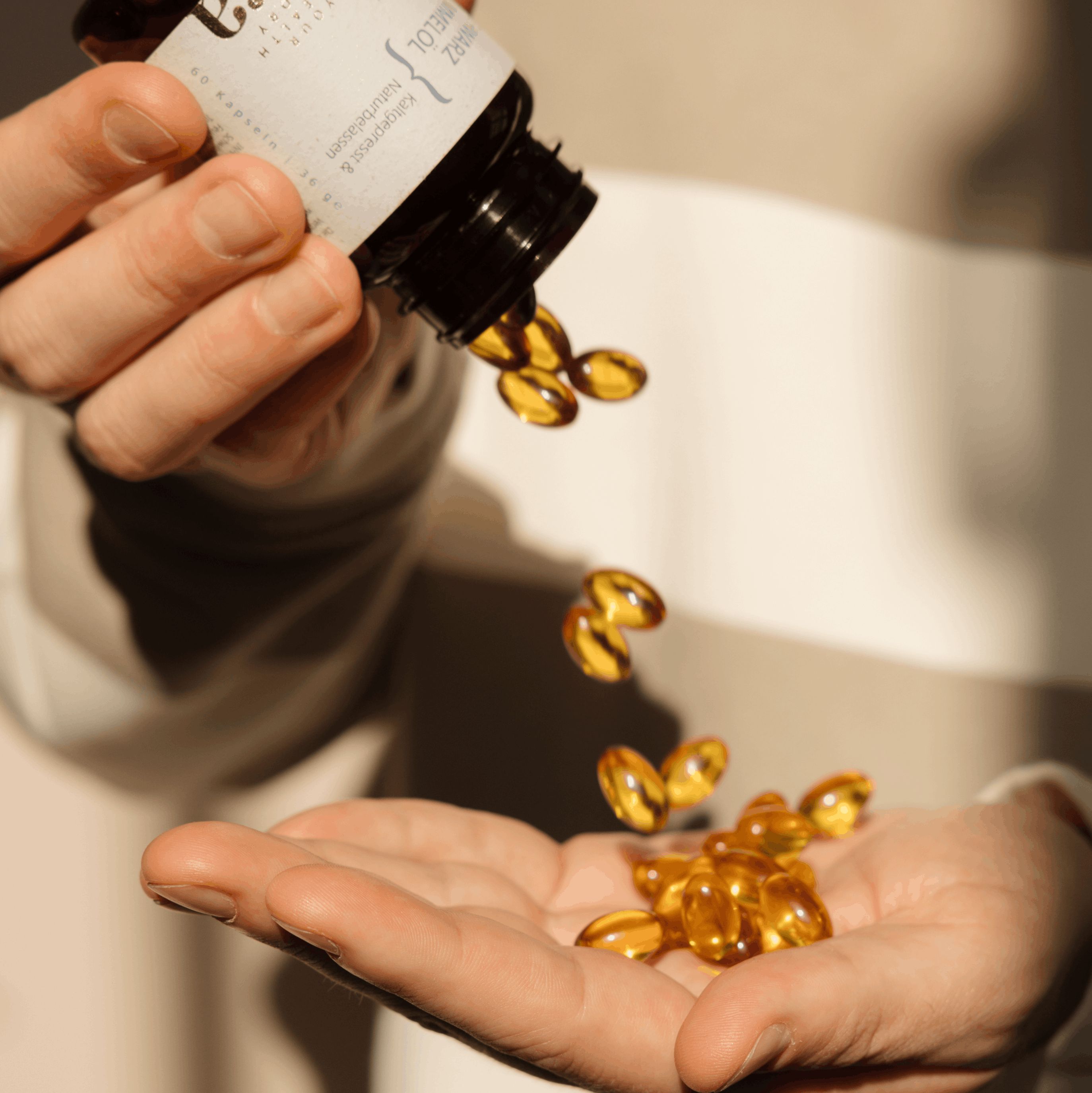 Handen gieten amberkleurige capsules uit een flesje in een handpalm.