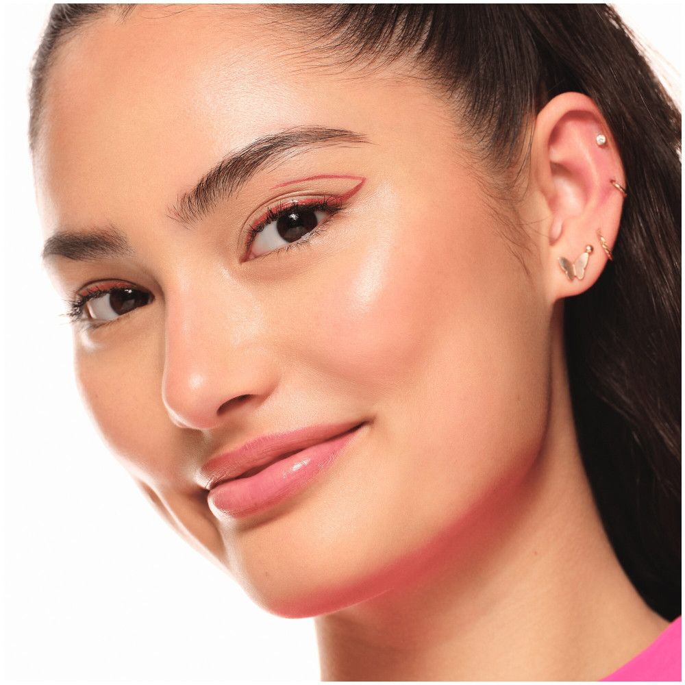 Gros plan d'une femme avec un eye-liner rose. Elle porte des boucles d'oreilles et sourit.