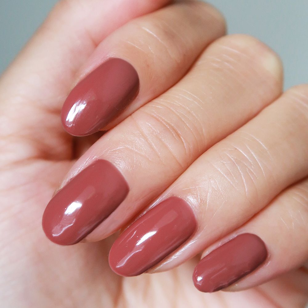 Main avec ongles peints en rouge rouille. Les ongles sont de forme ovale.