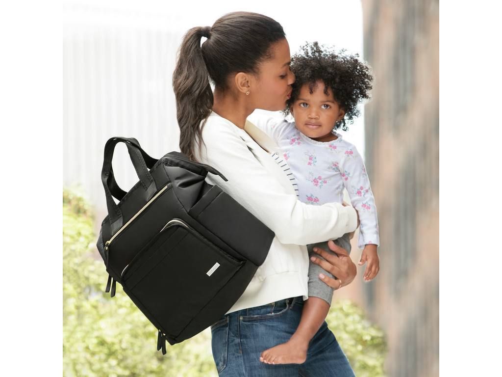 Zwarte luiertas op de schouder van een vrouw. Ze houdt een kind vast. Goudkleurige ritsen.