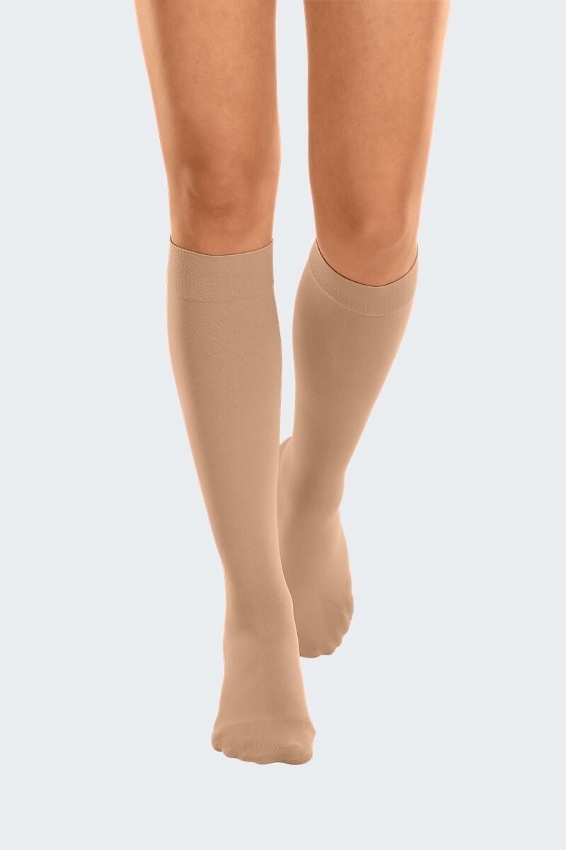 Bas de compression couleur chair, montants jusqu'aux genoux, portés sur les jambes. Matière fine et lisse. Vue de face.