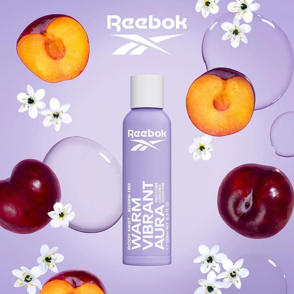 Spray corporel violet avec bouchon blanc. Texte: Warm Vibrant Aura, sans alcool. Entouré de prunes et de fleurs. Marque: Reebok.