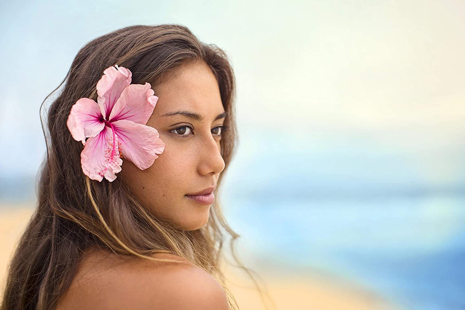 Jeune femme avec une fleur rose dans les cheveux, regardant de côté, fond de plage.
