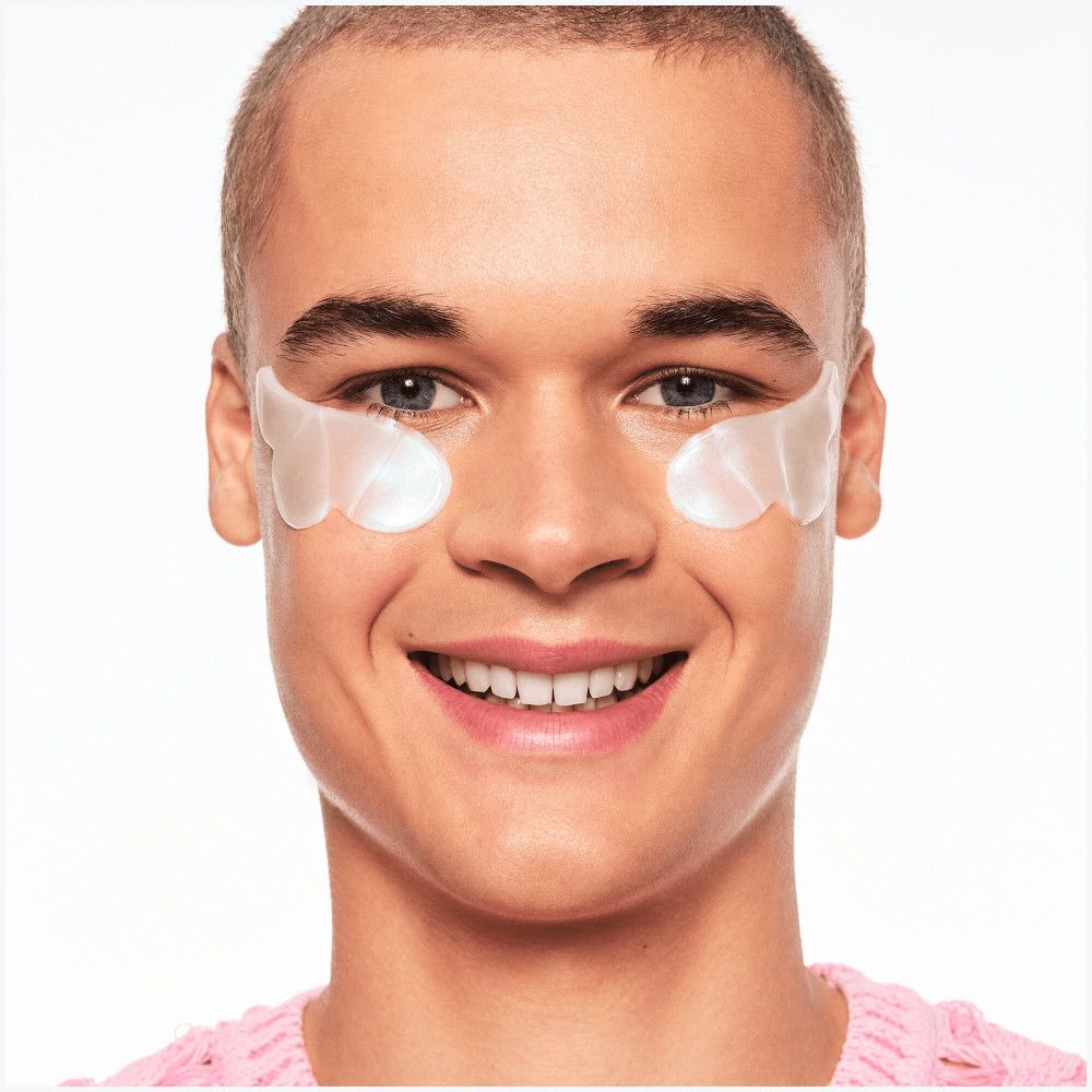 Homme avec patchs pour les yeux. Patchs blancs sur la peau sous les yeux. Sourit à la caméra.