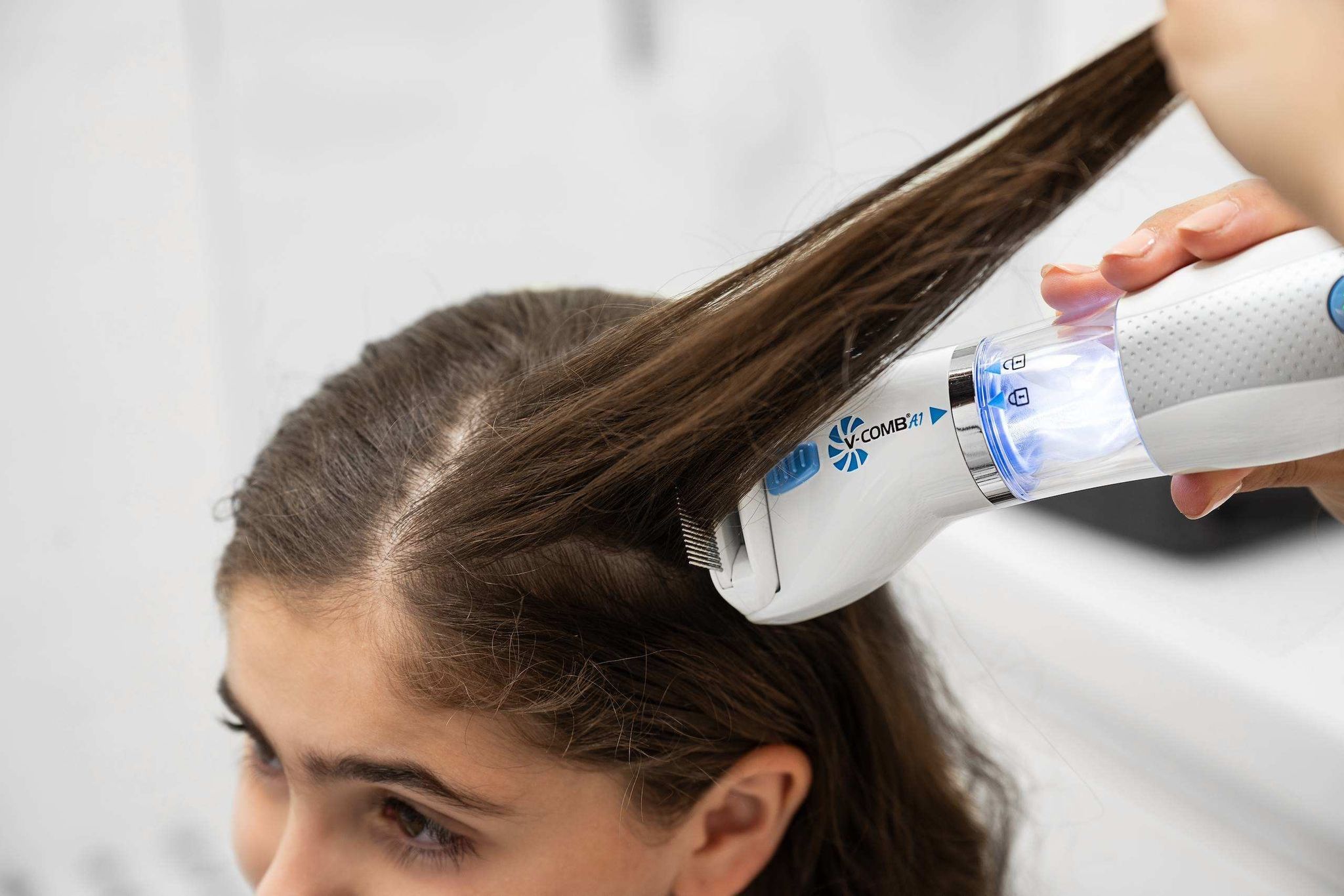 Peigne électrique anti-poux blanc et bleu utilisé sur les cheveux d'un enfant.