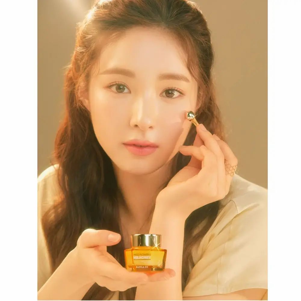 Vrouw houdt een gouden potje en een applicator vast. Opschrift: Miss Flower & Mr. Honey. Ze raakt haar oog aan met de applicator.