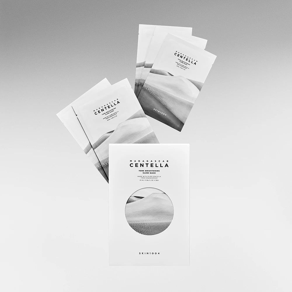 Productverpakking en maskerzakjes. Opschrift: MADAGASCAR CENTELLA. Merk: SKIN1004. Meerdere zakjes zweven boven de verpakking.