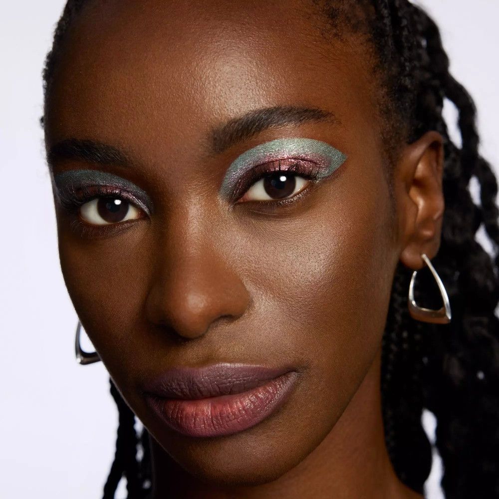 Gros plan d'un visage maquillé. Yeux avec fard à paupières bleu-rouge. Peau foncée, lèvres foncées, boucles d'oreilles argentées.