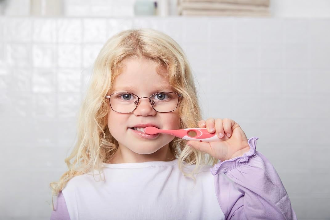 Jeune fille portant des lunettes se brosse les dents avec une brosse à dents rose. Arrière-plan de salle de bain.