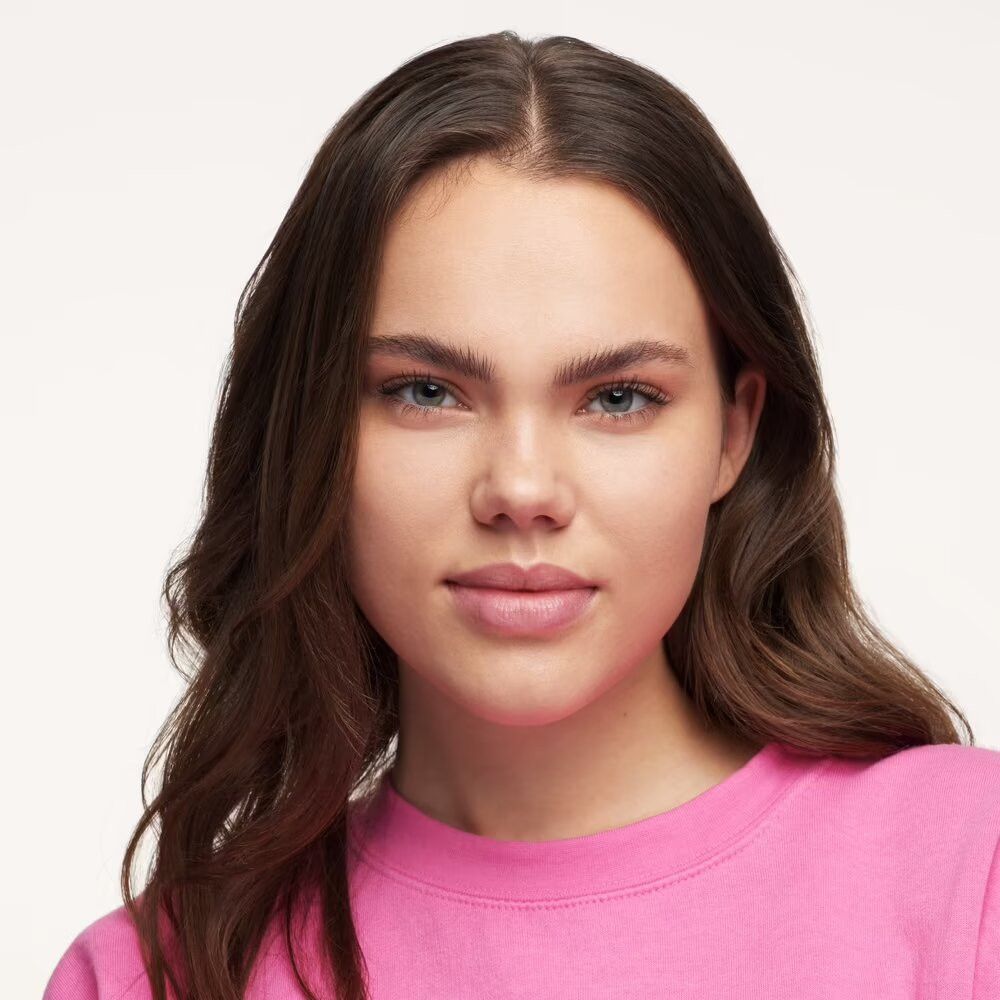 Portrait d'une jeune femme portant un haut rose. Elle regarde directement la caméra.