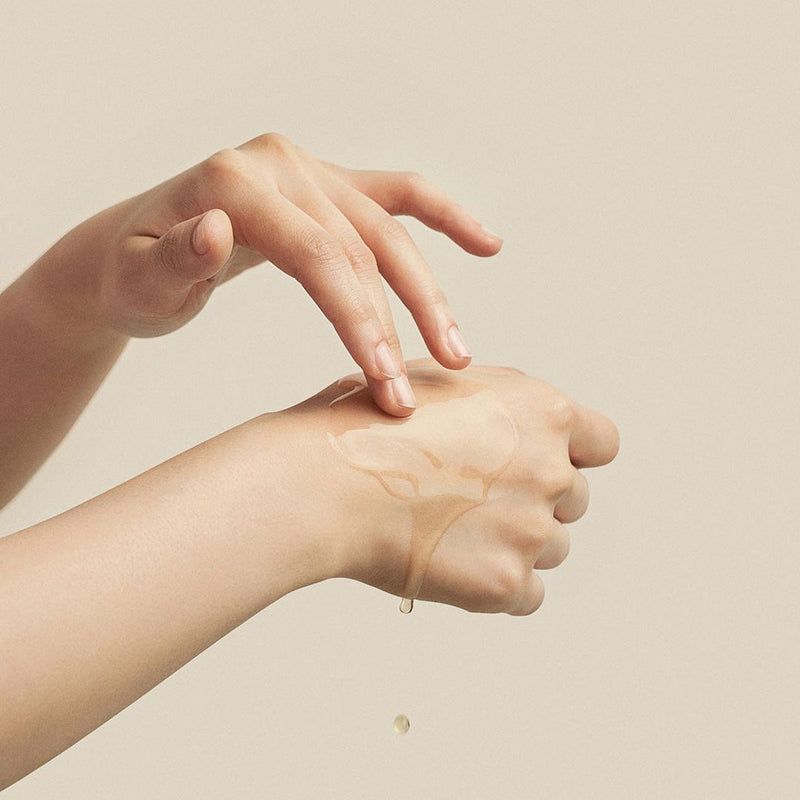 Handen die vloeistof op de handpalm aanbrengen. Vloeistof druppelt. Geen productaanduiding zichtbaar.