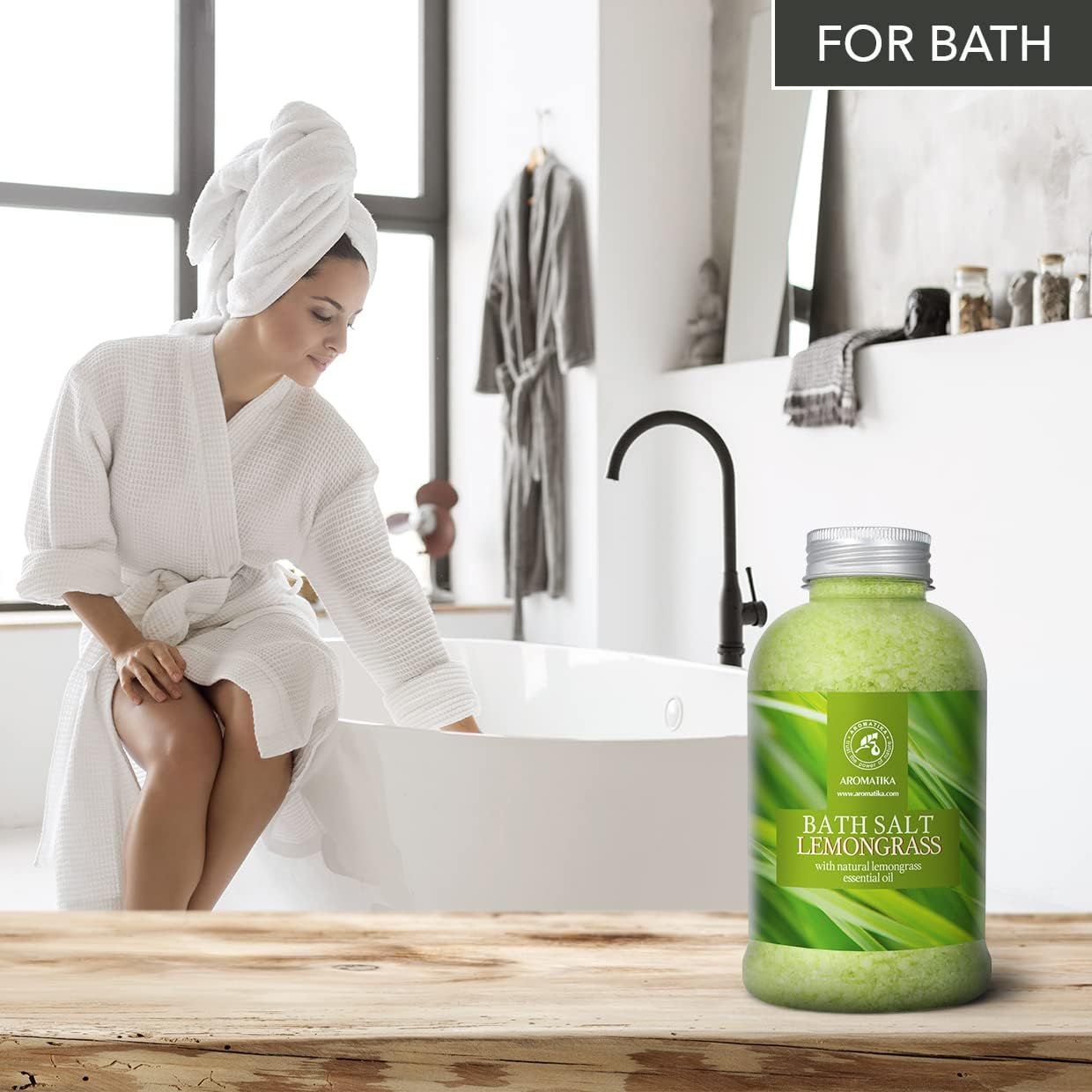 Femme en peignoir et serviette sur la tête assise au bord de la baignoire. AROMATIKA Sel de bain Lemongrass à côté.