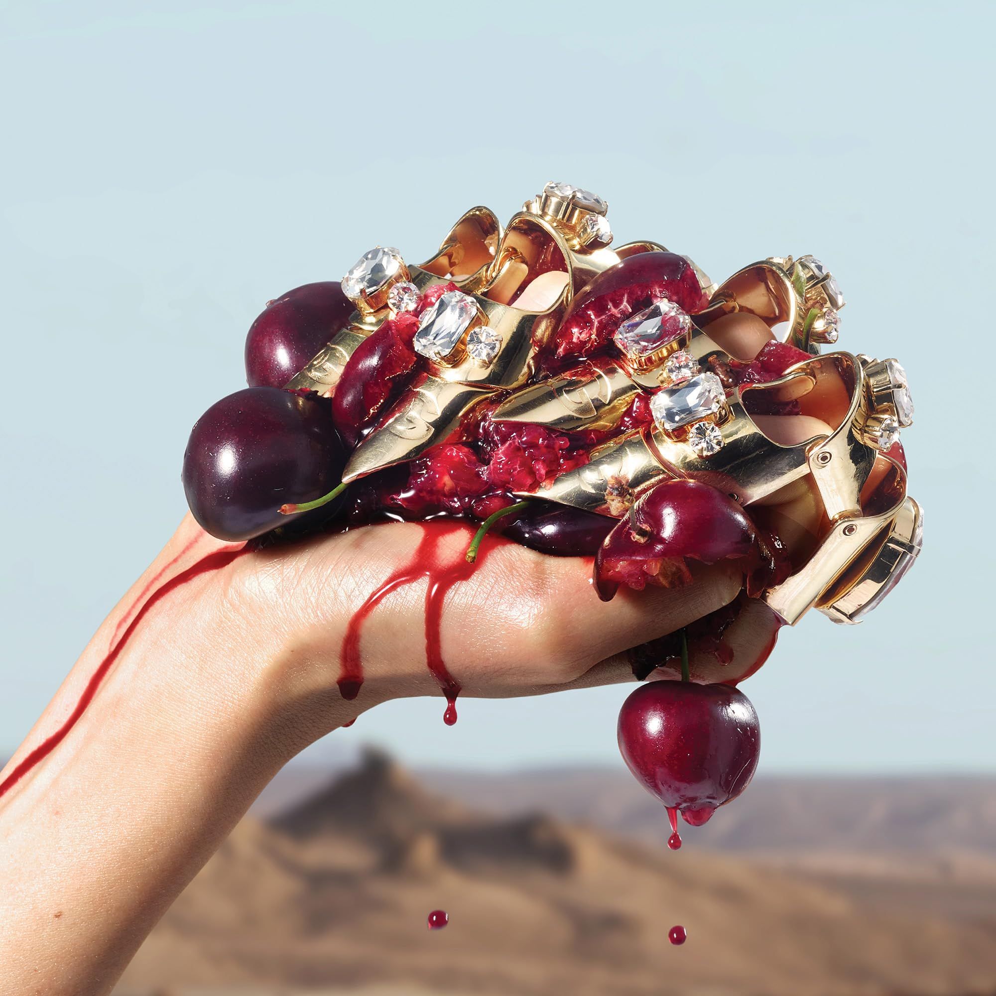 Hand houdt kersen en gouden ringen met diamanten vast. Rood sap druppelt. Achtergrond: landschap.