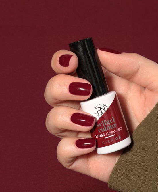 Main avec ongles vernis rouge profond. Flacon de vernis à ongles avec logo PN et inscription: selfgel colour, N°055 deep red.