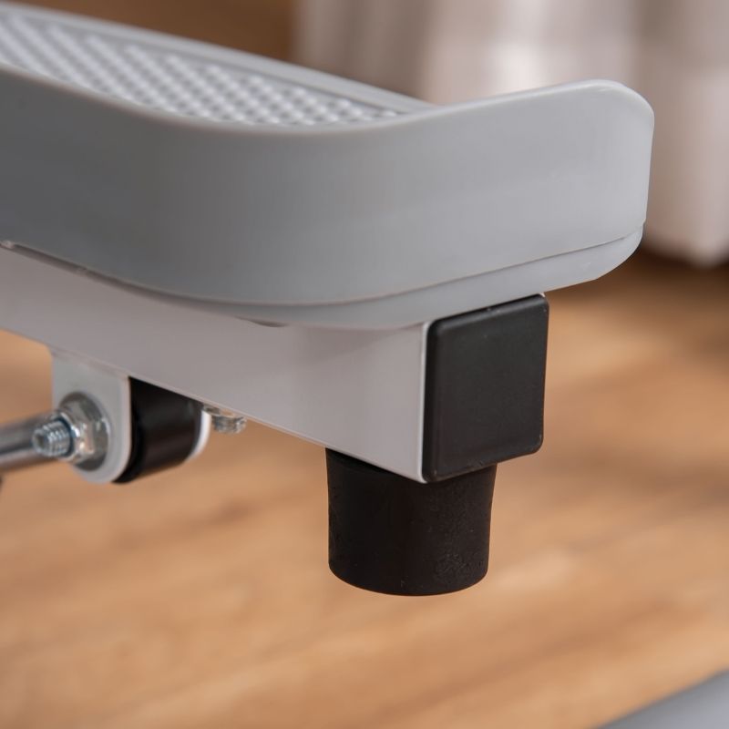 Grijze stepper-voet met zwarte rubberen voet. Grijs voetstuk. Wit metalen frame. Houten vloer.